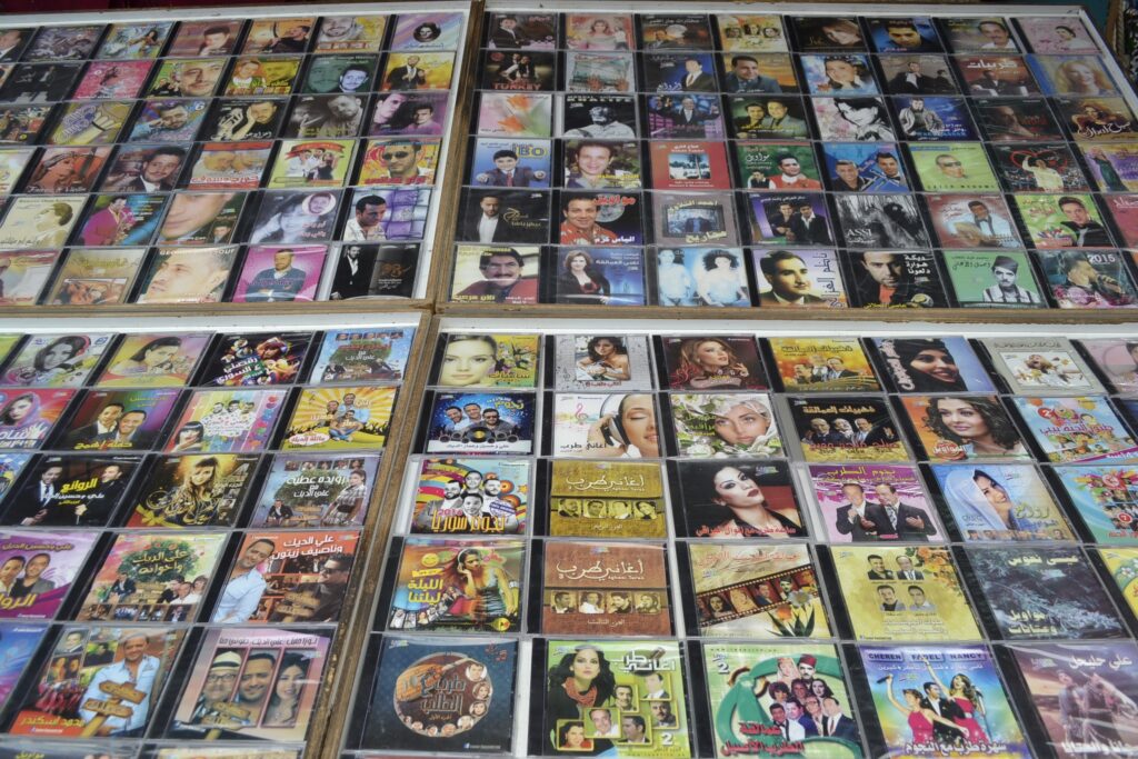 Rows of various movie and music DVD and CD cases on display for sale, with covers displaying titles in Arabic.