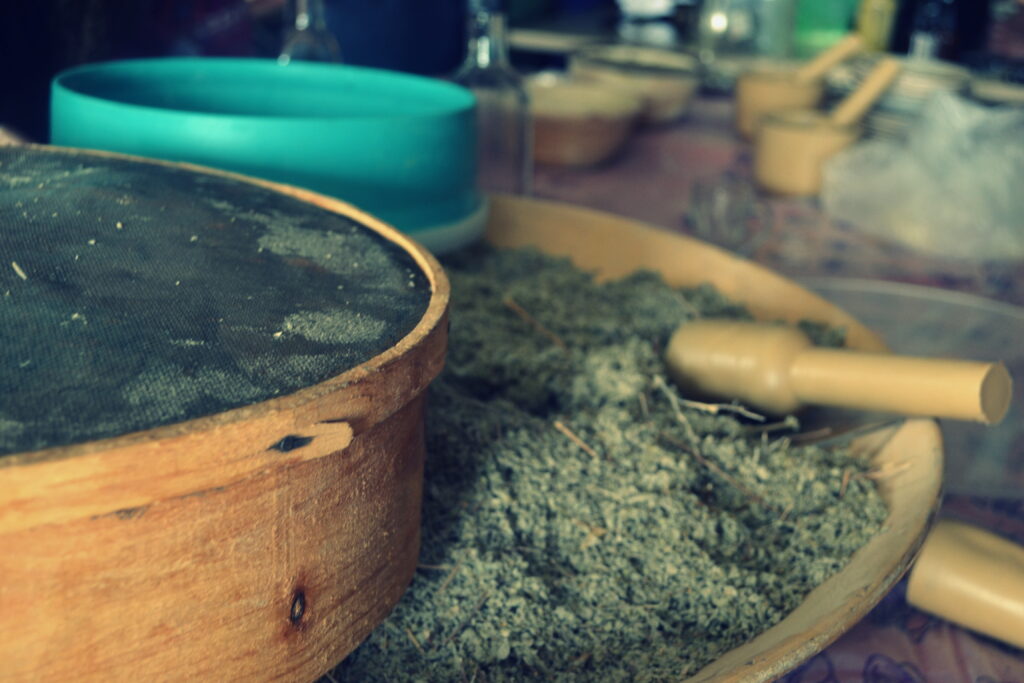 A large platter of spices with a pestle in the foreground, and several mortars and pestles in the background.